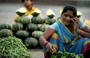 An Indian vegatable seller arranges vegatables as she speaks on a cellular phone at a roadside vegatable market in Allahabad