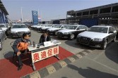 Two salesmen sit beside new cars for sale at a dealership in Beijing on March 29, 2009.