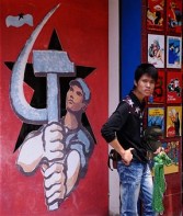 street vendor hawks souvenir items next to a shop selling communist propaganda posters in the ancient quarter of Hanoi.