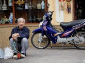 An elderly man sits waiting for clients next to an air-pump for motorcycles and bicycle tires, on the pavement of a street in Hanoi'